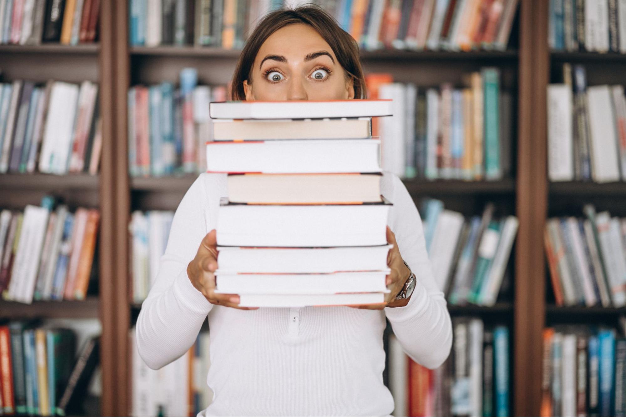 a female student with eyes wide open holding eight books in her hands at the library