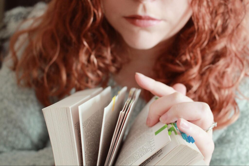 a red-haired girl with a serious facial expression looking through a book